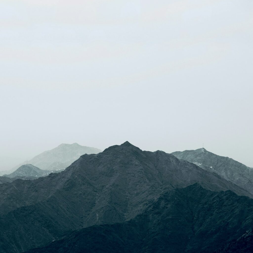 Ett disigt bergslandskap med flera mörka, taggiga toppar mot en blek, mulen himmel. Den lugna scenen framkallar färgpsykologi, eftersom det mjuka, diffusa ljuset och de dämpade färgerna skapar en lugn atmosfär. winwinweb